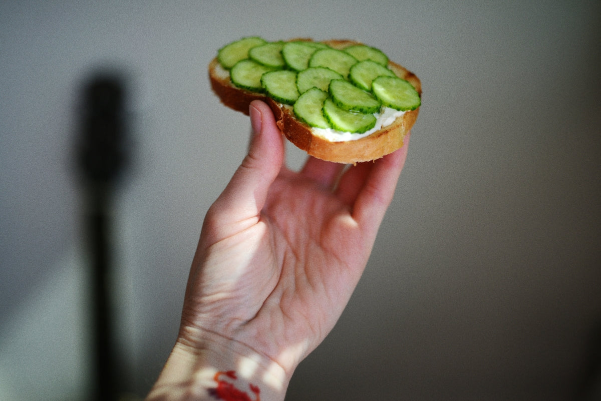 a person holding a sandwich with cucumbers on it