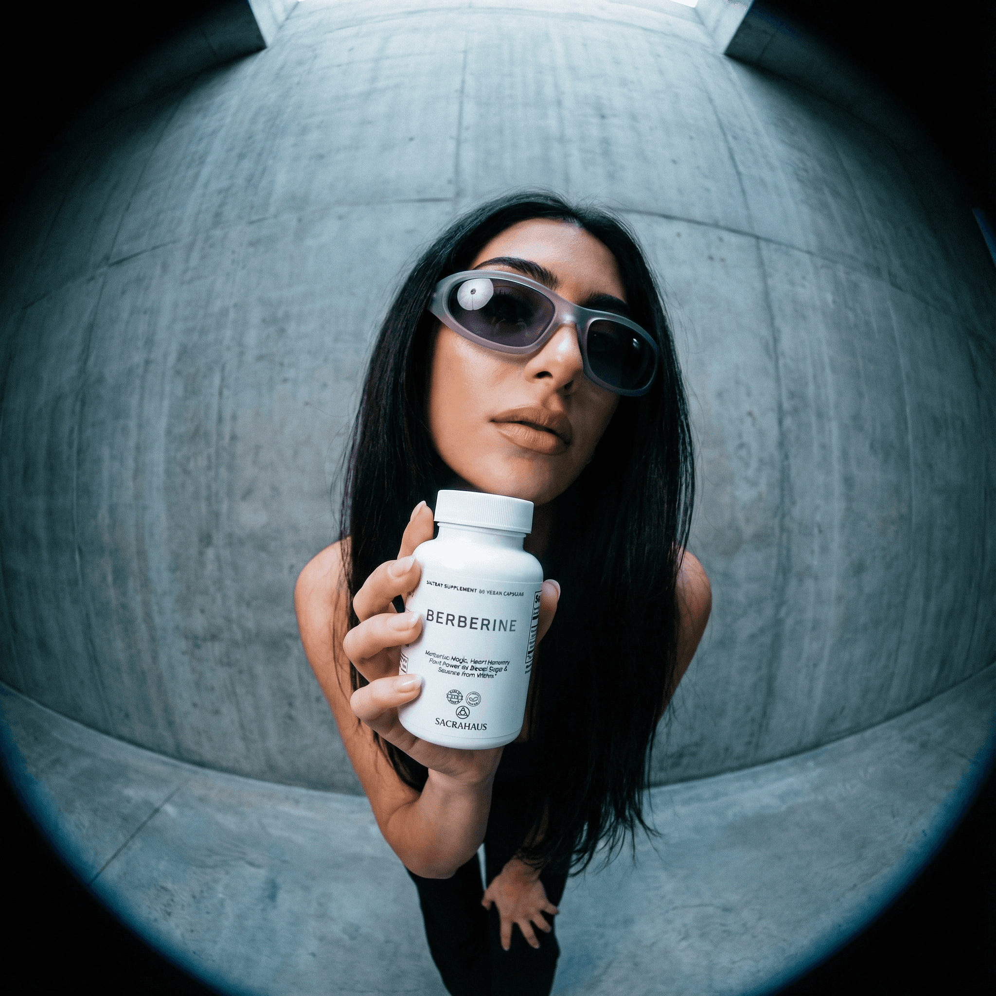 SACRAHAUS vegan berberine supplement bottle held by a model in stylish sunglasses against a concrete background