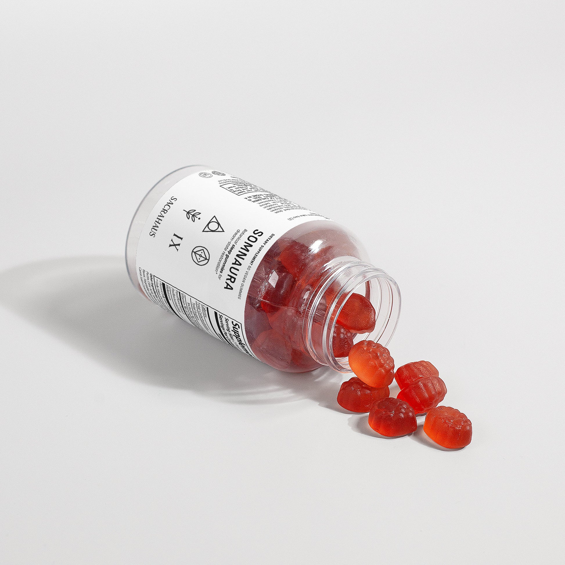 SACRAHAUS vegan sleep gummies bottle spilling red gummy supplements on white background