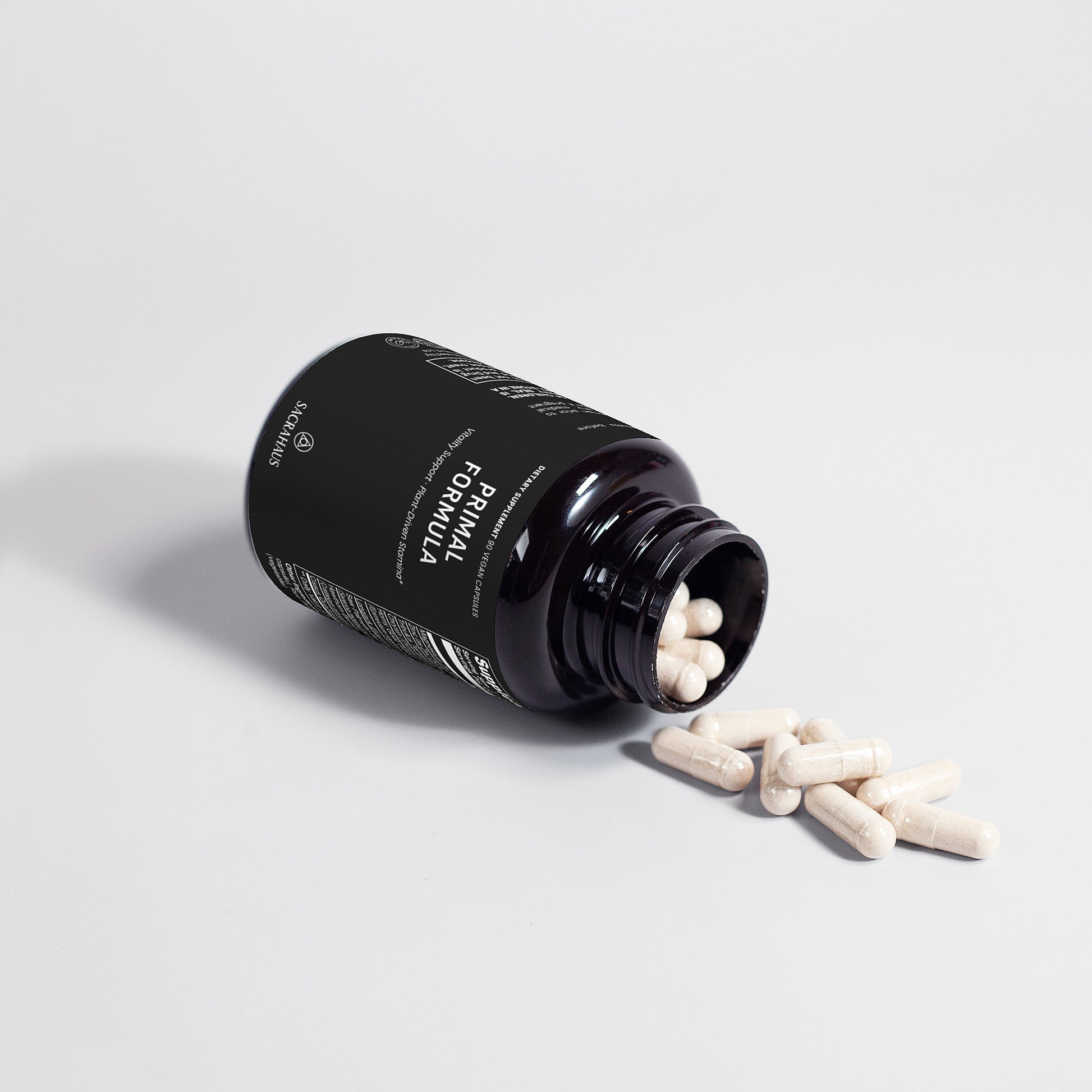 SACRAHAUS vegan supplements for men Primal Formula specialty supplement capsules spilling from black bottle