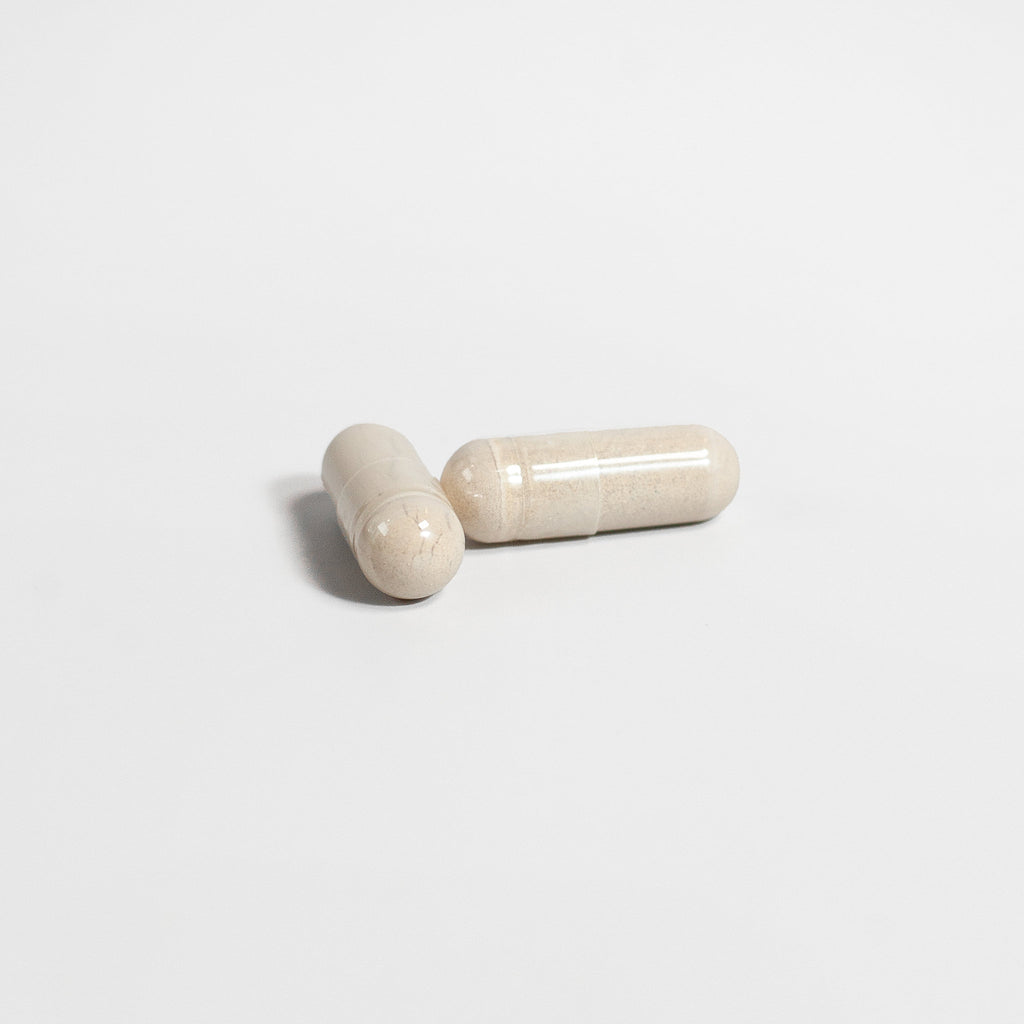 Two beige capsules of SACRAHAUS vegan supplements for men on white background