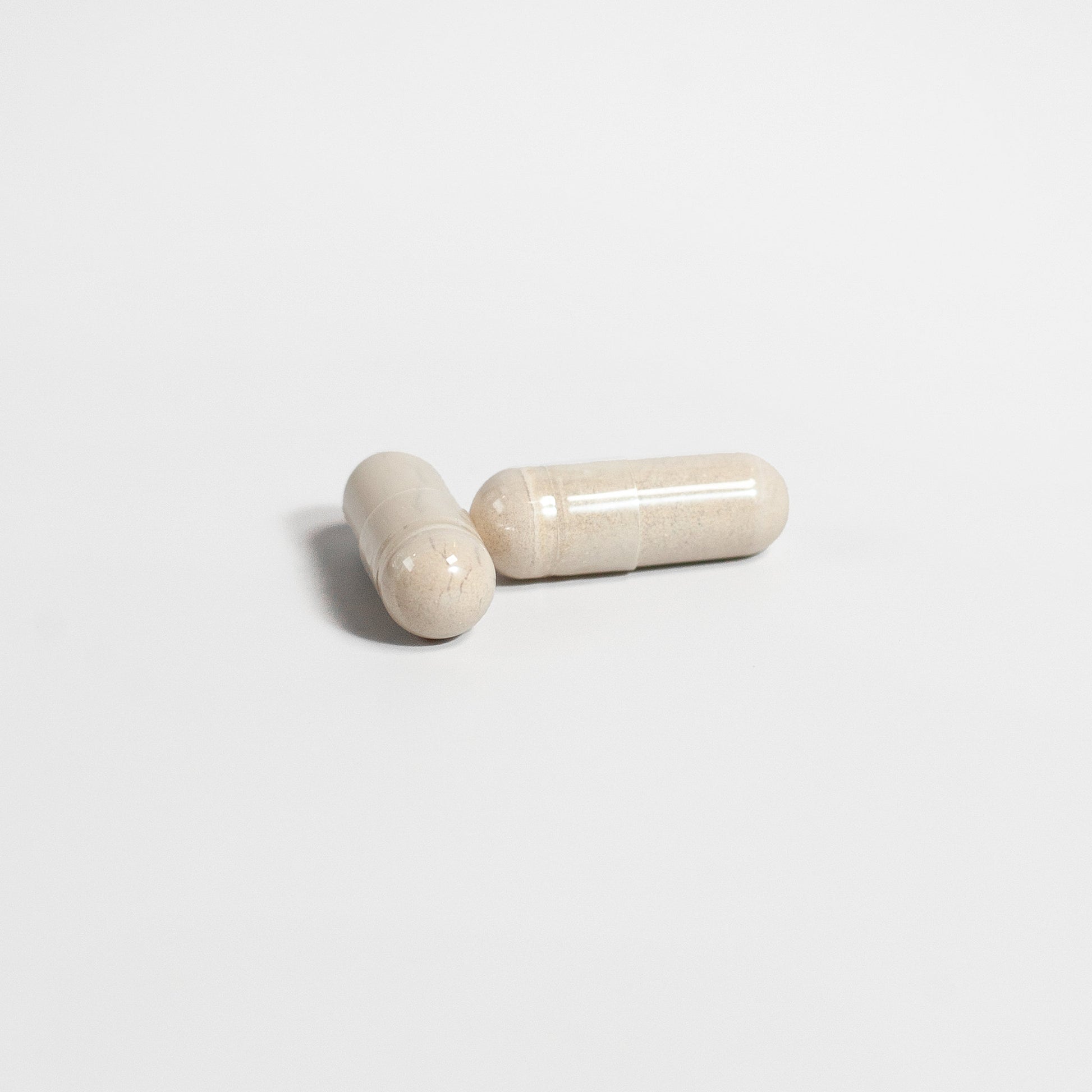 Two beige capsules of SACRAHAUS vegan supplements for men on white background